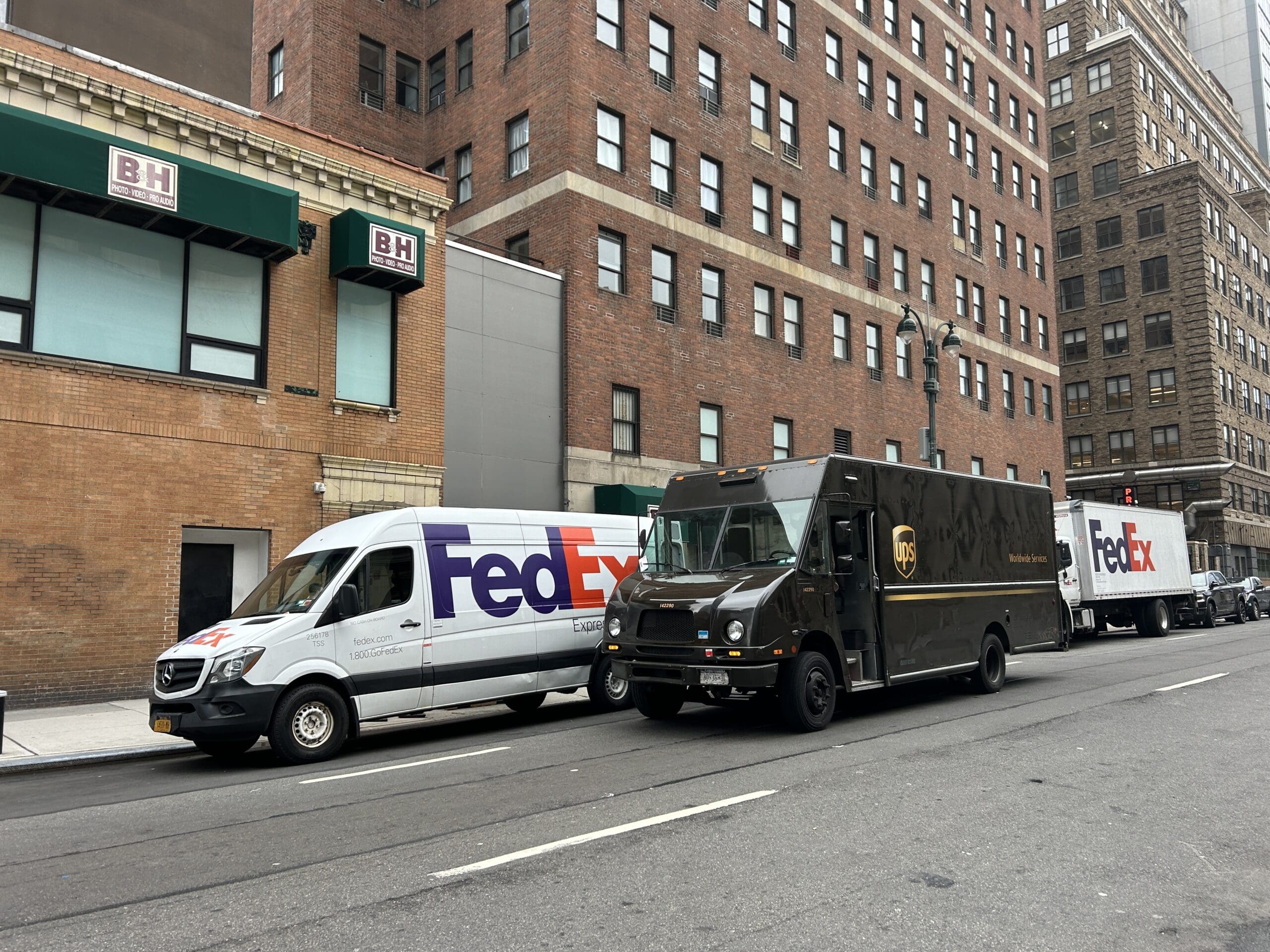 FedEx and UPS delivery trucks double-parked on a busy New York City street, highlighting last mile delivery congestion and emissions challenges addressed by Smart Package Room systems sustainable package logistics solutions