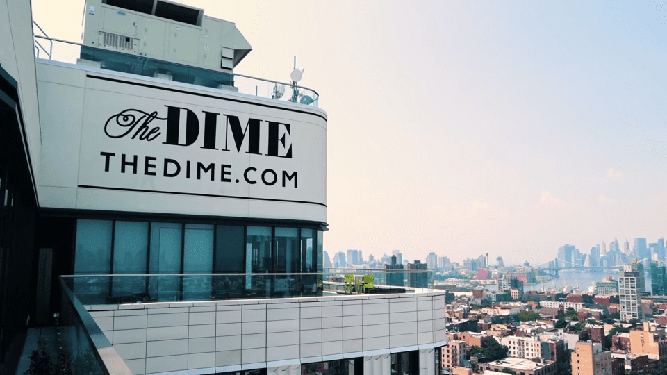 Exterior view of The Dime apartment building featuring its rooftop signage and panoramic city skyline, representing modern multifamily living supported by advanced package management solutions.