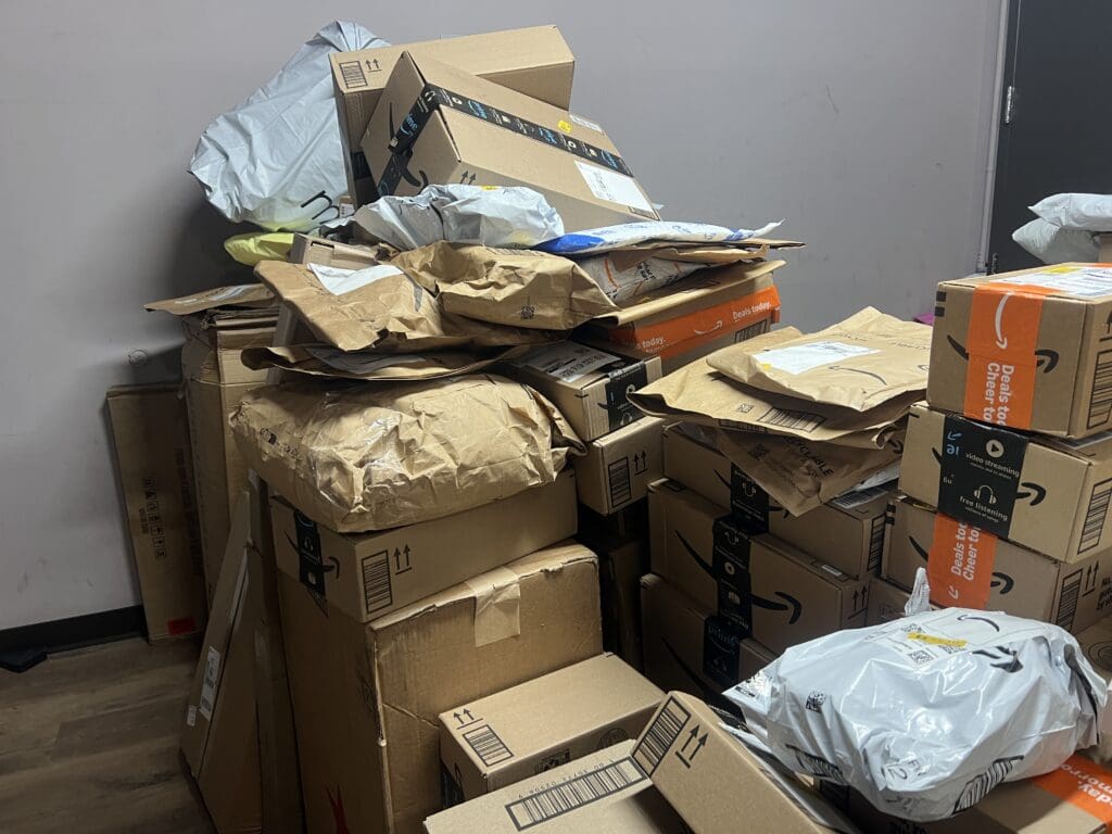 Overflowing piles of delivered packages in a residential mailroom, showing the challenges of streamlining package delivery in residential buildings without an automated package management system.
