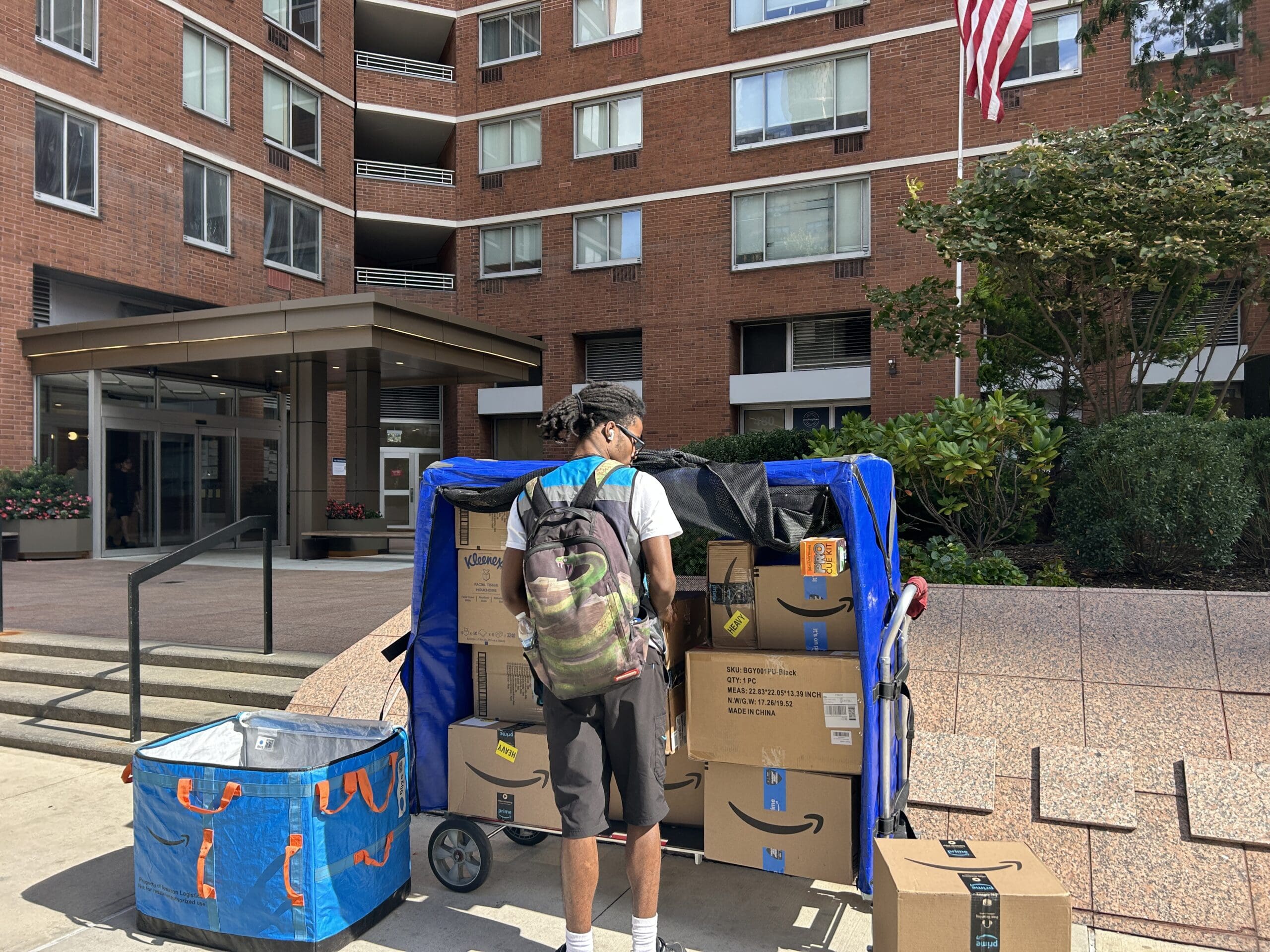 Courier unloading a high volume of packages outside a multifamily residential building, highlighting how to streamline package delivery in residential buildings during peak delivery periods.