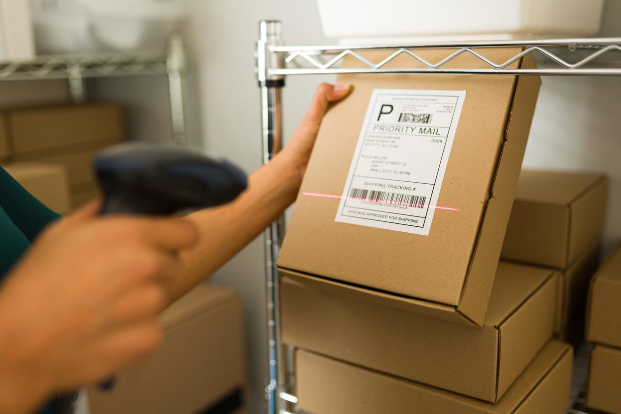 Courier scanning a package label on open shelving inside a Smart Package Room system during the digital intake process.