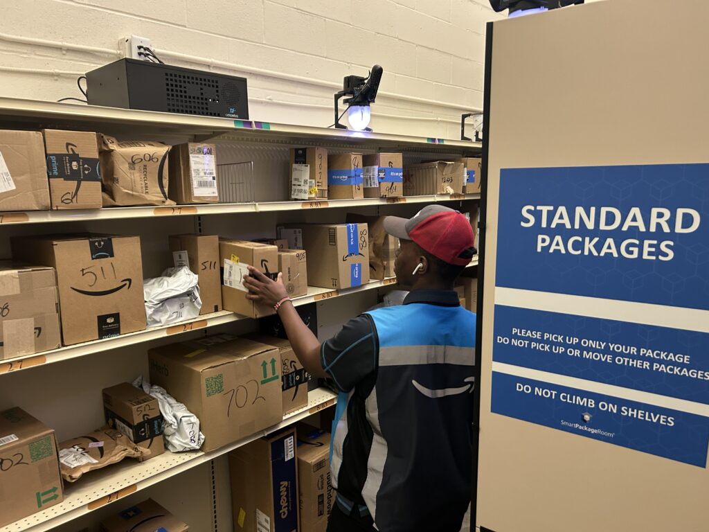 Amazon courier engaged in apartment package management placing a package onto a labeled standard package shelf inside a Smart Package Room