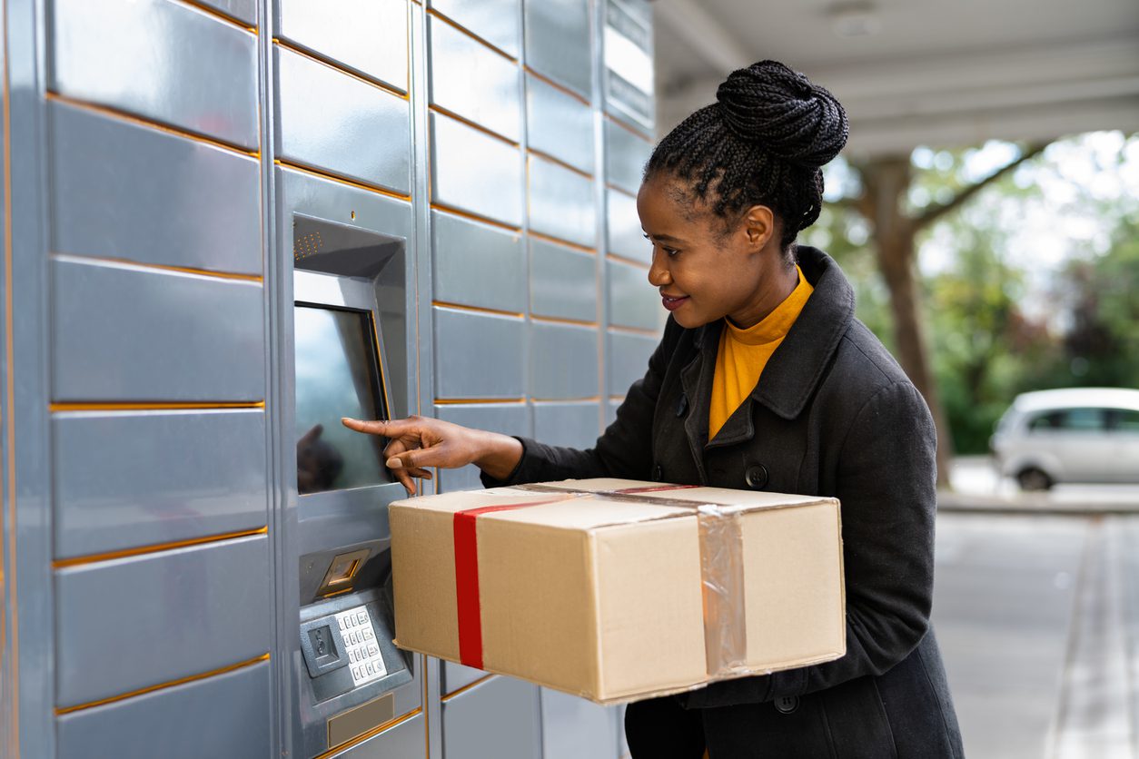 IMG_5127 Apartment resident holding a cardboard package while using a touchscreen self-service package locker kiosk outdoors