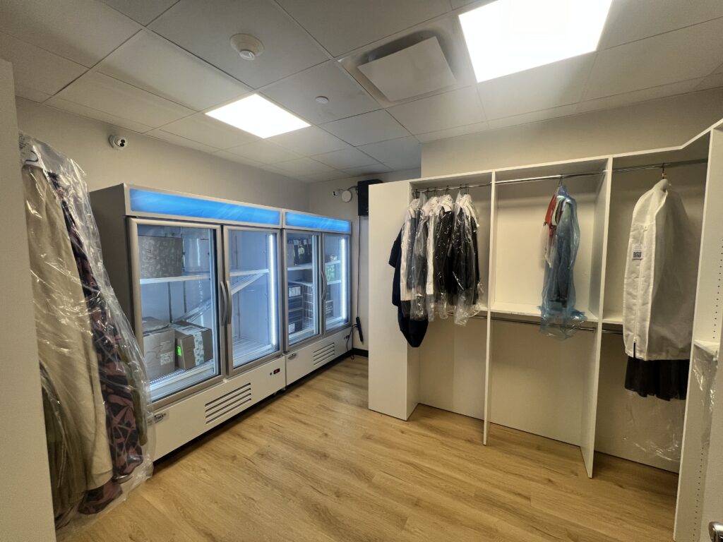 Smart package room interior showing dry cleaning garment storage with hanging clothes in plastic wrap and illuminated cold storage refrigerators for resident delivery