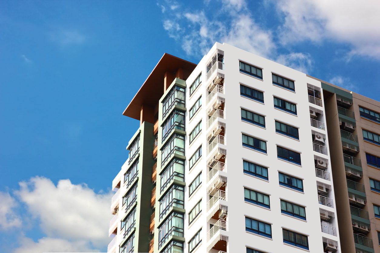 IMG_5127 Exterior of a modern high-rise apartment building with multiple balconies and floor-to-ceiling windows against a blue sky