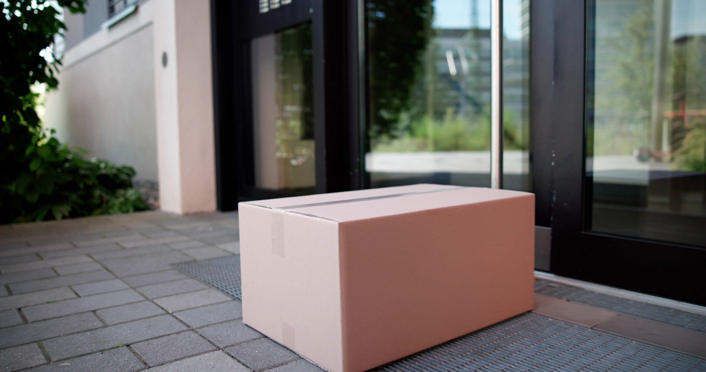 Cardboard package left unattended on the doorstep outside a glass multifamily apartment building entrance
