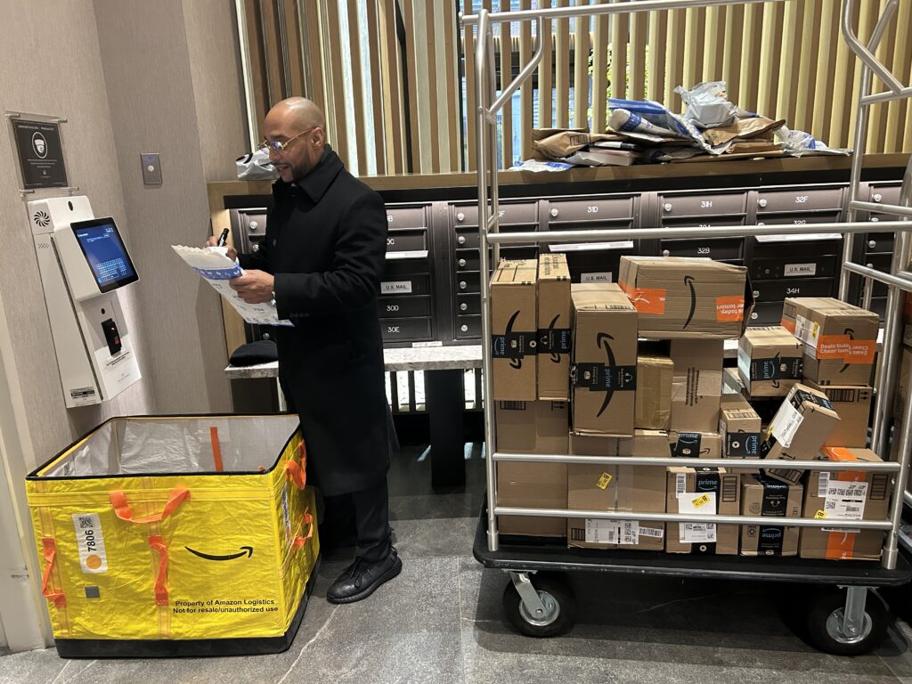 Property staff member sorting packages next to a cart stacked with mail deliveries in an apartment package room