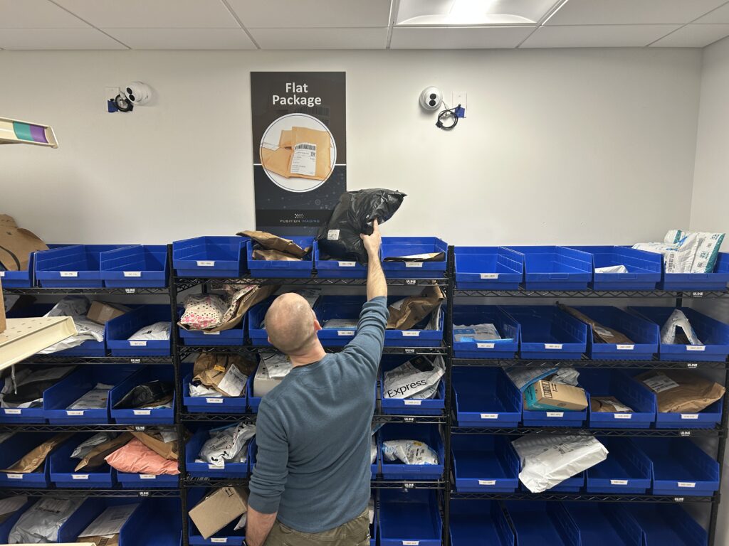 Apartment resident picking up a flat package from a labeled blue bin inside an apartment package room