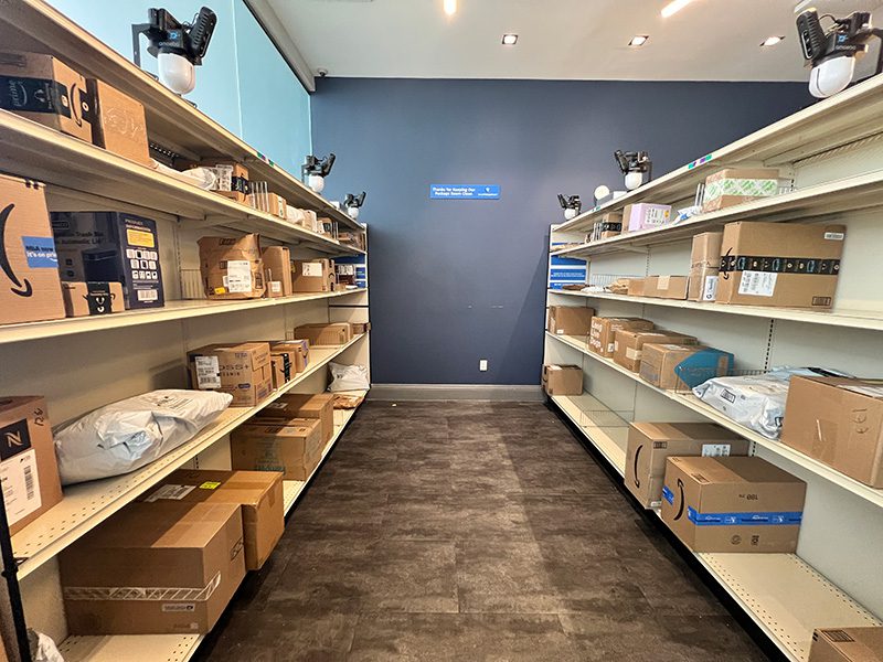Amoeba Modules mounted above two rows of open shelves stocked with parcels inside a Smart Package Room system.