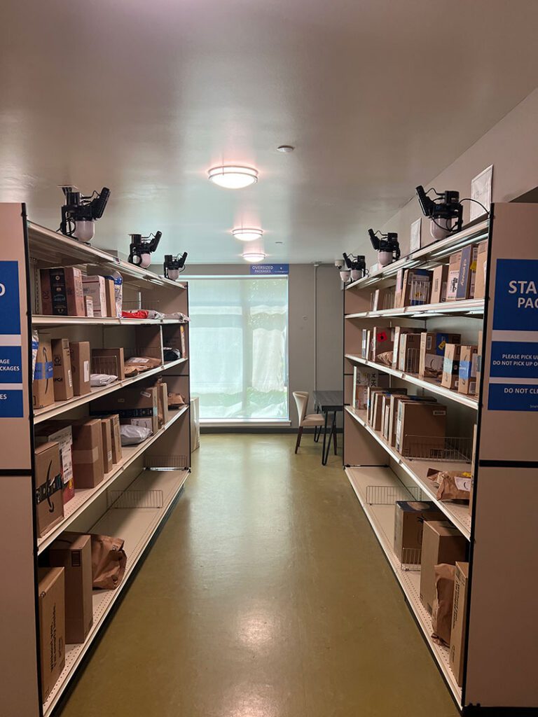 Smart Package Room system aisle of open shelving with resident parcels and shelf-mounted Amoeba Modules.