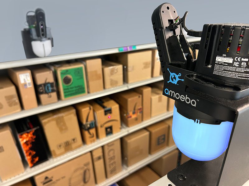 Close-up of an Amoeba Module with blue light guiding a laser dot to a package on an apartment shelf
