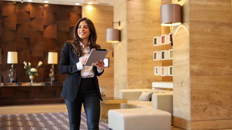 IMG_5127 Luxury apartment concierge holding a tablet while walking through an upscale lobby seating area.