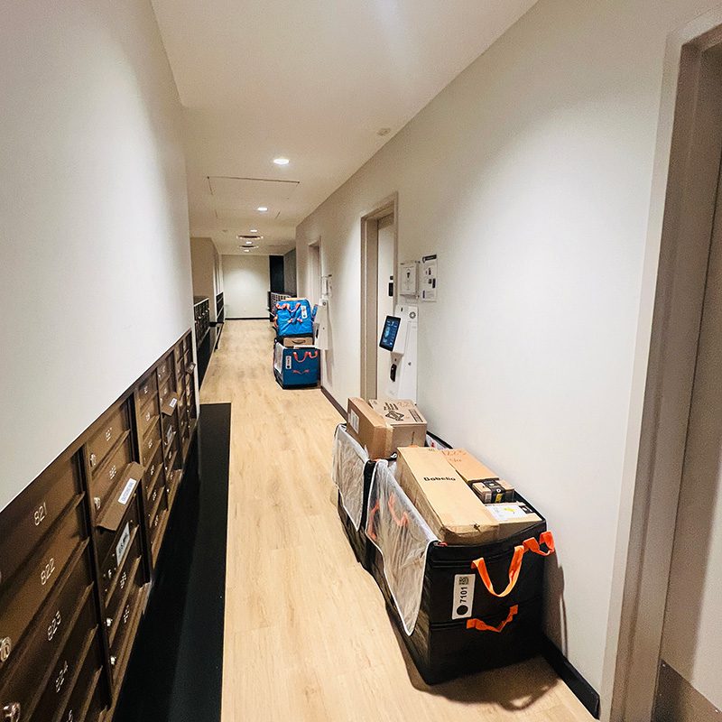 Delivery totes of packages stacked on the floor beside a resident mailbox wall in a high-rise apartment corridor.