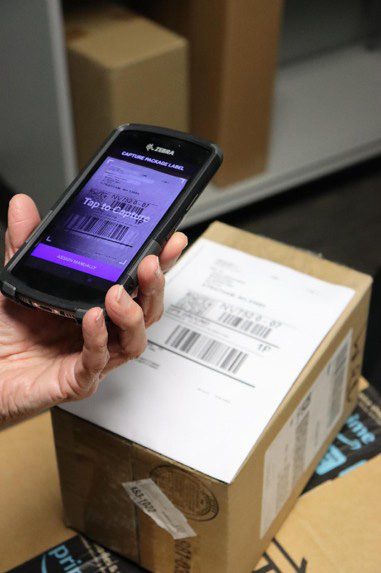 Handheld scanner reading ‘Tap to Capture’ held over a shipping label as parcel is logged on arrival.